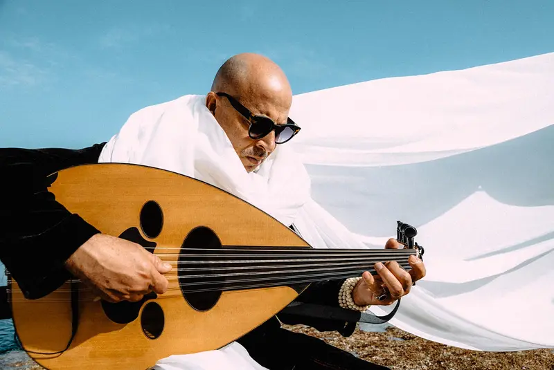 Dhafer Youssef holding an oud in front of billowing white fabric