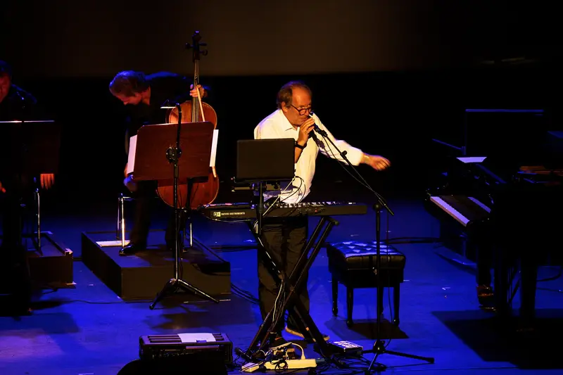 Hans Zimmer playing keyboards on a dimly lit stage with musicians behind him