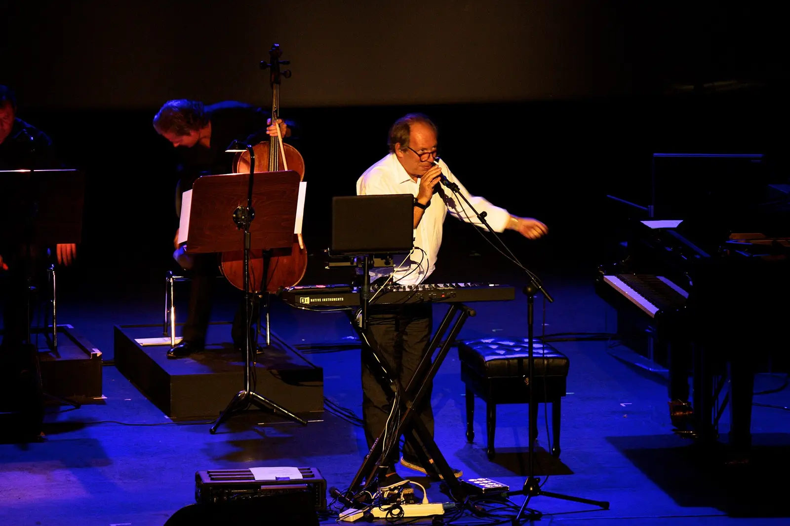 Hans Zimmer playing keyboards on a dimly lit stage with musicians behind him