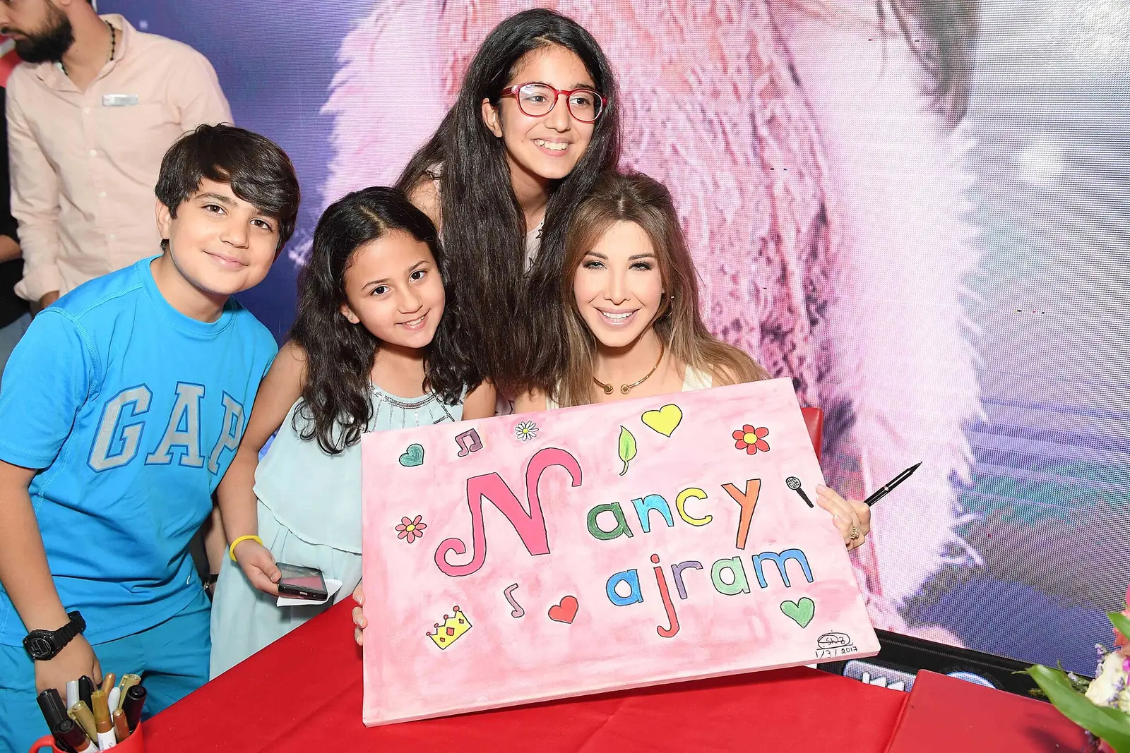 Nancy Ajram posing with young fans who hold a pink sign