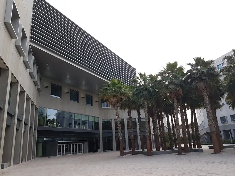 The glass-fronted NYU Abu Dhabi building on Saadiyat Island with palm trees in front