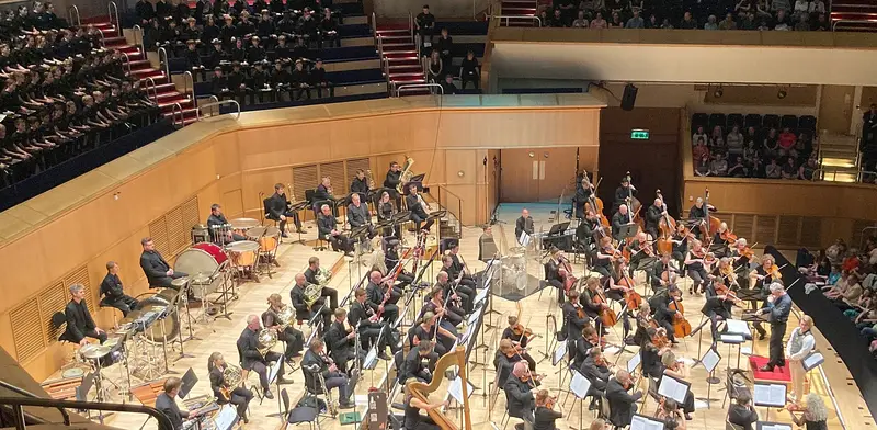 A symphony orchestra performing on the wooden stage of a concert hall before a seated audience