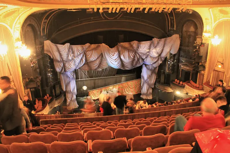 The orange-seated auditorium and draped stage curtain of a Broadway theatre during The Phantom of the Opera