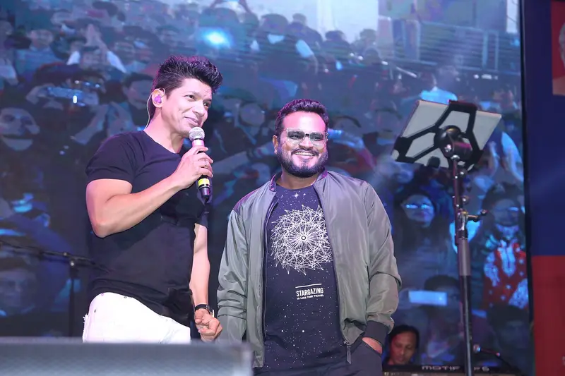 Shaan holding a microphone on stage beside Rishikesh Pandey at a live show in Indore