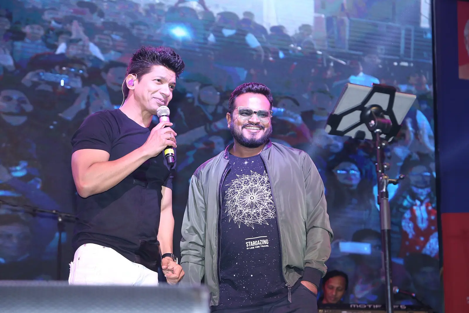 Shaan holding a microphone on stage beside Rishikesh Pandey at a live show in Indore
