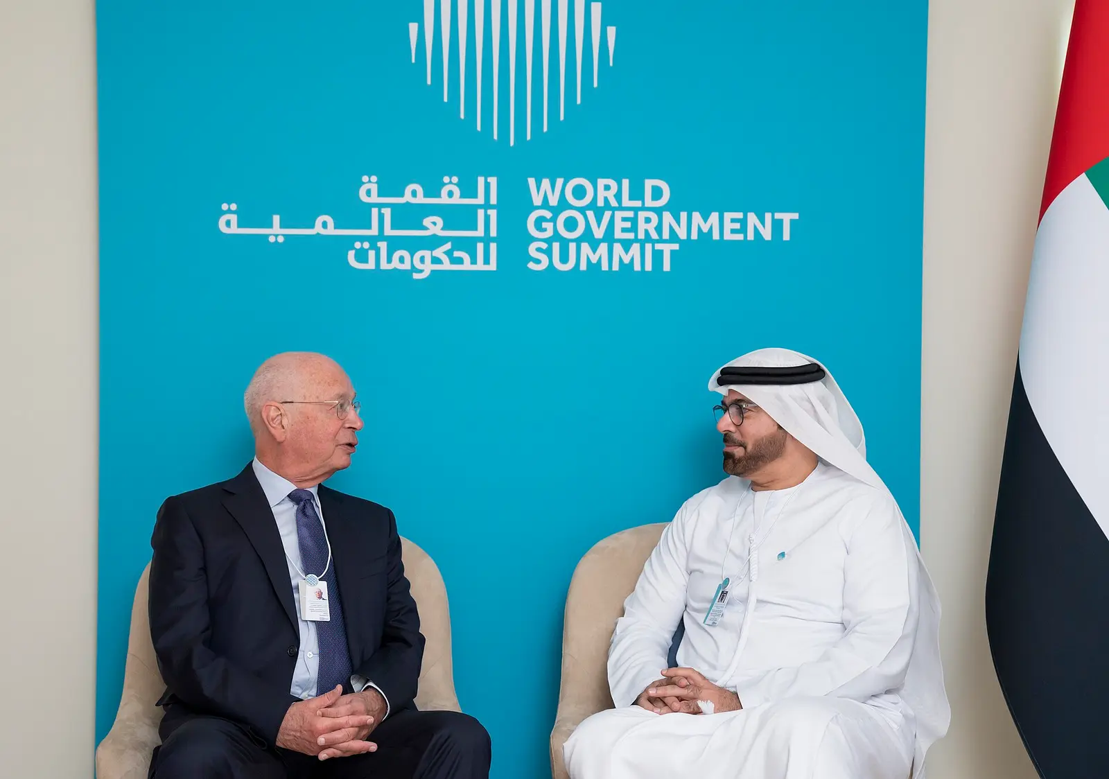 Two men in conversation in front of the World Government Summit backdrop