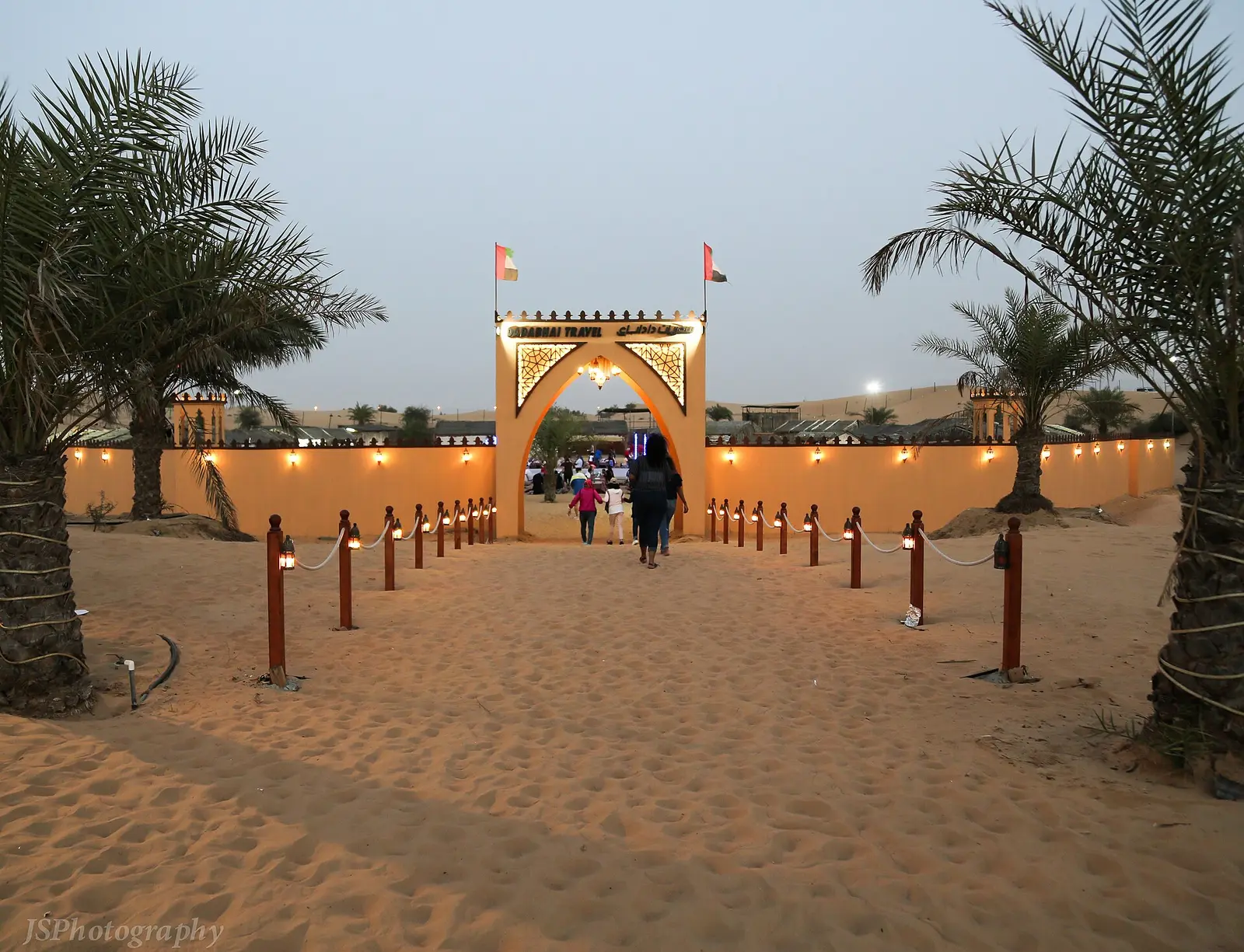 The arched entrance to a desert camp between palm trees at dusk