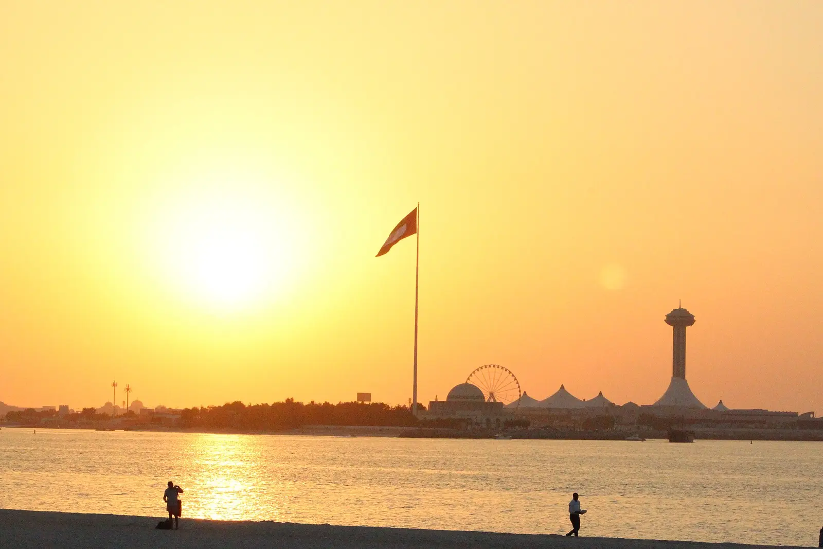 Sun setting over the water at Abu Dhabi Corniche with a flagpole on the skyline