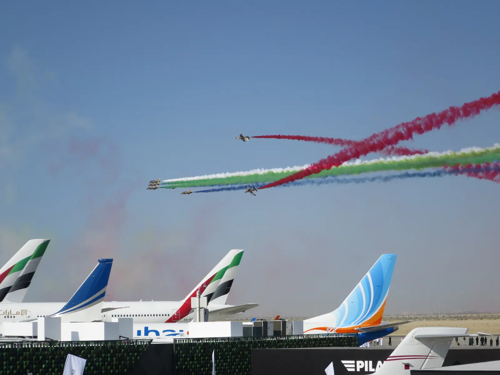 The Al Fursan aerobatic team trailing coloured smoke over airliners at the Dubai Airshow in 2023