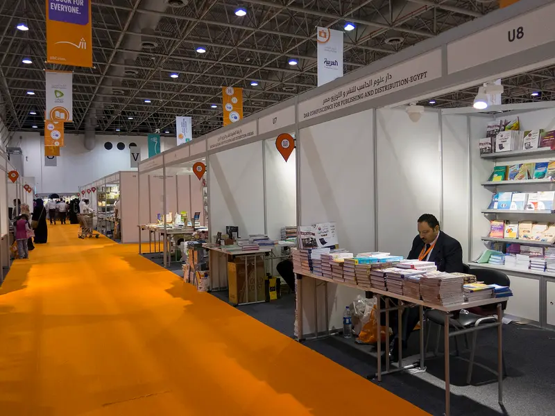 A stand-lined aisle with orange carpet inside a hall at Expo Centre Sharjah during the book fair in 2014