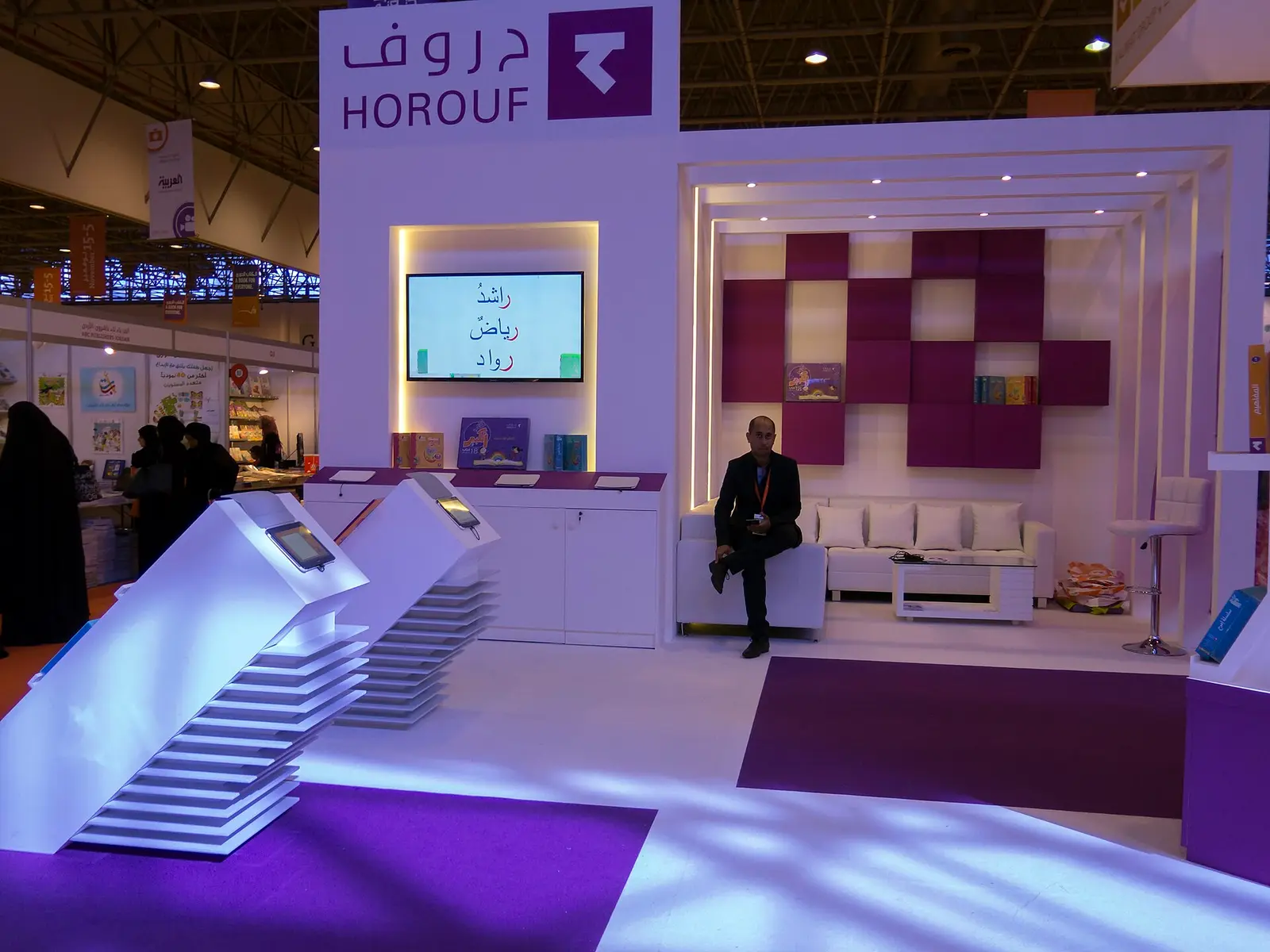 A lit purple publisher stand inside an exhibition hall at Expo Centre Sharjah in 2014
