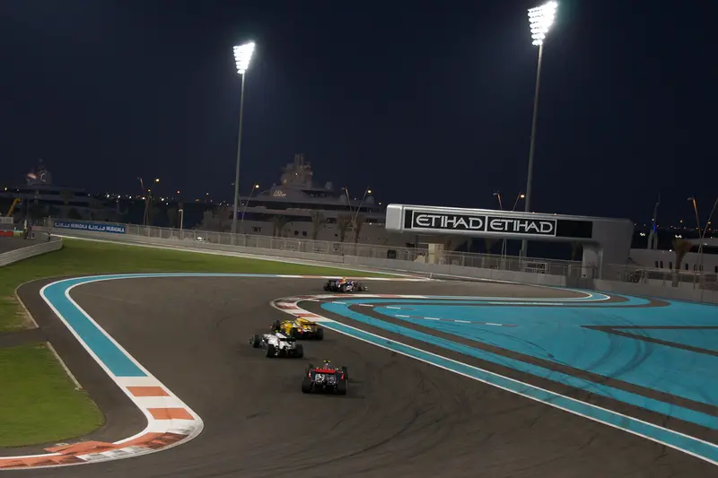 Cars racing through a floodlit corner of Yas Marina Circuit at night